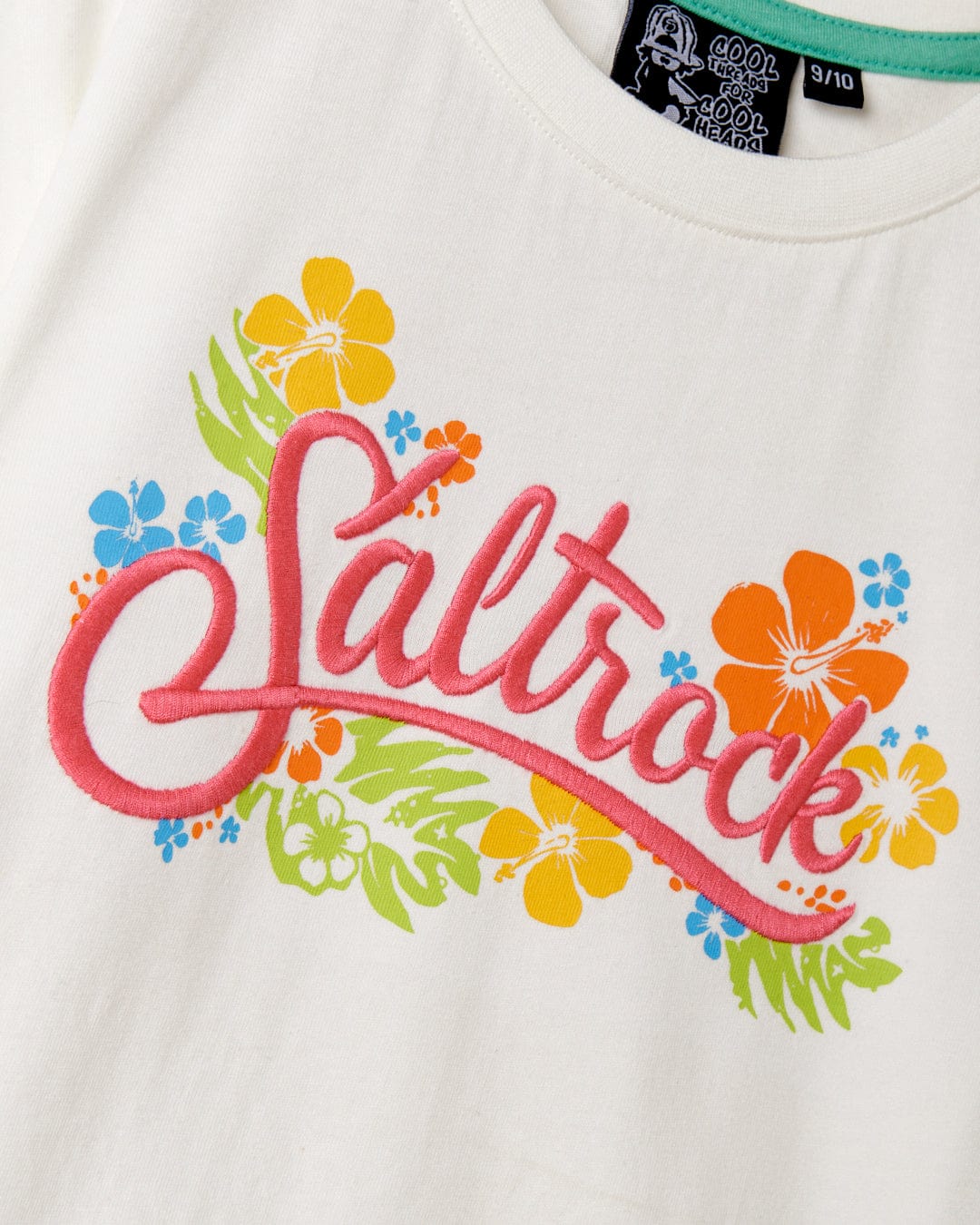 Detail of a white Tropic - Recycled Kids Short Sleeve T-Shirt with the Saltrock print in pink, surrounded by colorful floral designs.