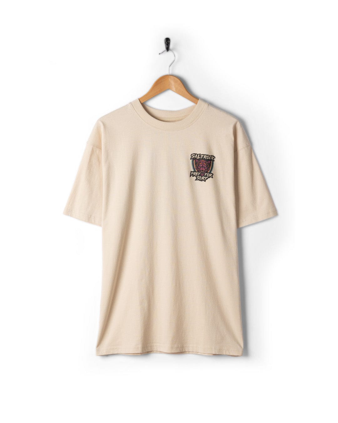 The Saltrock Wolfscale II men's oversized short sleeve t-shirt in cream, made from 100% cotton with a small graphic and text on the left chest, is displayed on a wooden hanger against a white background.