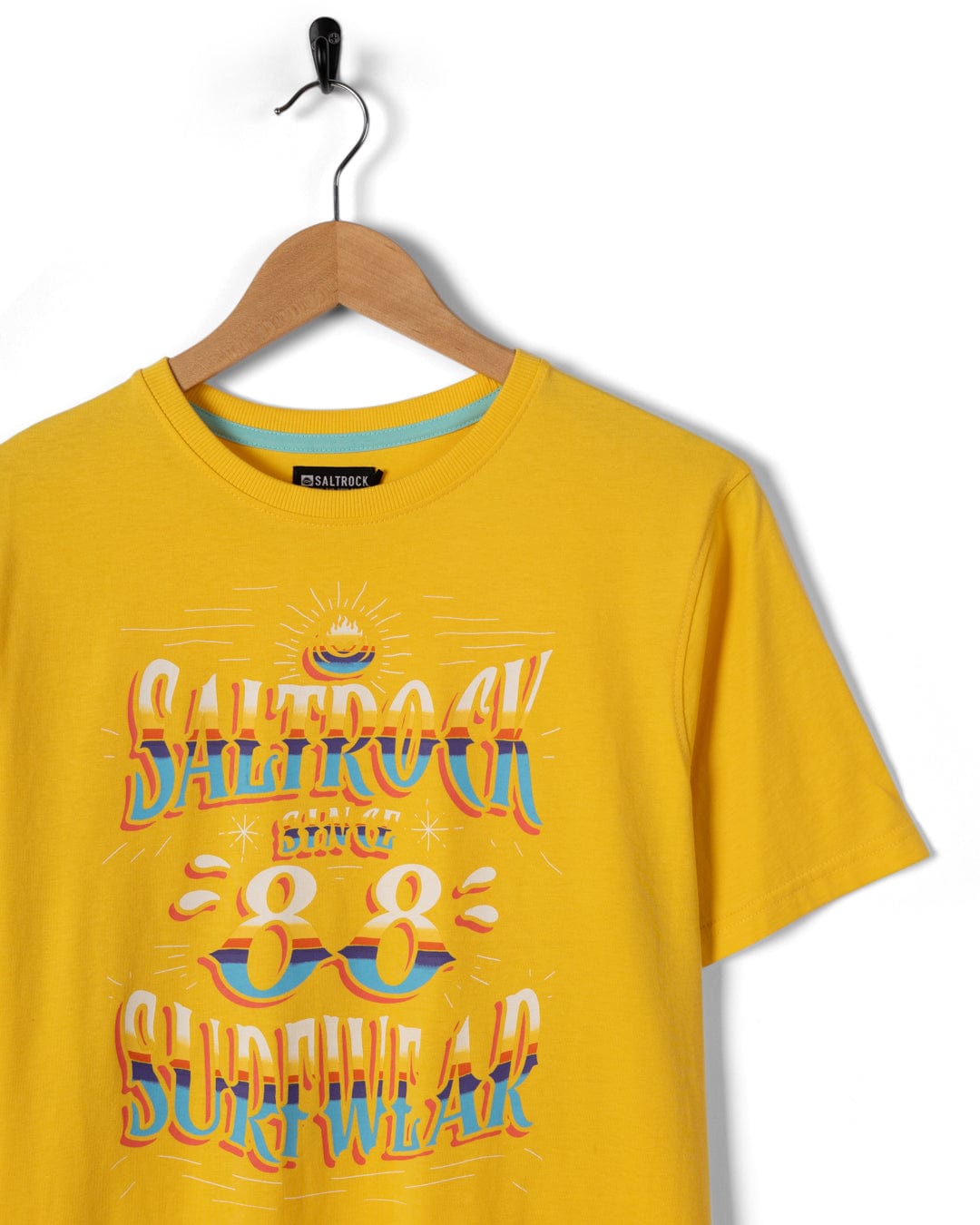 The yellow Mex Logo men's t-shirt by Saltrock hangs on a wooden hanger, showcasing bold Saltrock branding and "Saltrock 88 Surfwear" in colorful, stylized letters on the front.