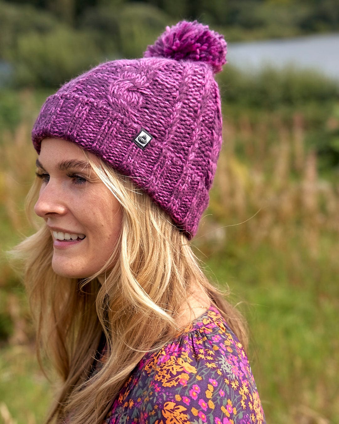 A woman wearing a Saltrock Twist - Cabled Beanie - Dark Pink with a pom pom.