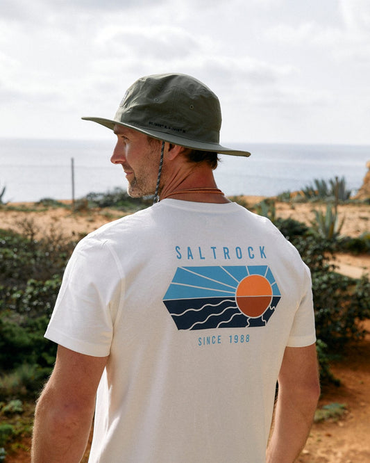 A man wearing a Saltrock Green Gaitor bucket hat and a t-shirt with the "Saltrock since 1988" logo on the back looks out towards a coastal landscape.