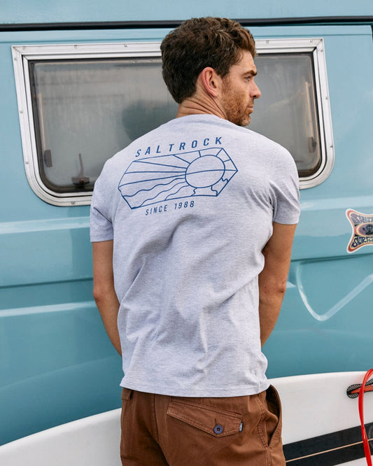 A man wearing a grey Saltrock Vantage Outline - Mens Short Sleeve T-Shirt, with graphic branding, standing next to a camper van.