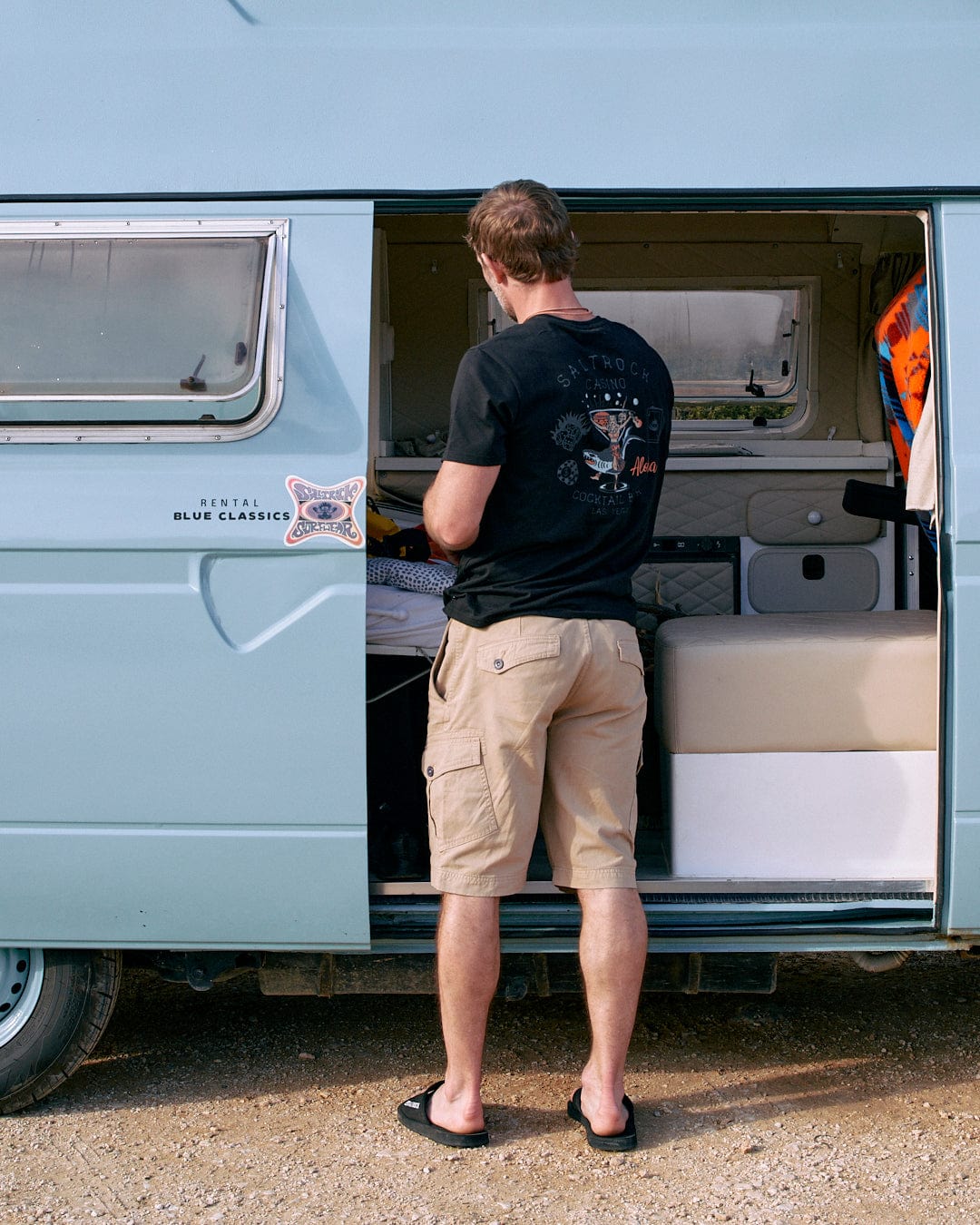 A man opening the door of a black Saltrock Vegas Cocktail - Mens Short Sleeve T-Shirt - Black camper van.