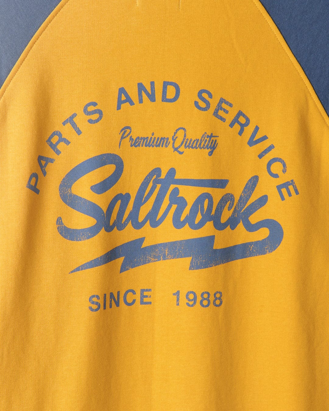 Close-up of a yellow Saltrock Vegas Script - Mens Pop Raglan Hoodie with raglan sleeves and the text "parts and service, premium quality, since 1988" printed in blue.
