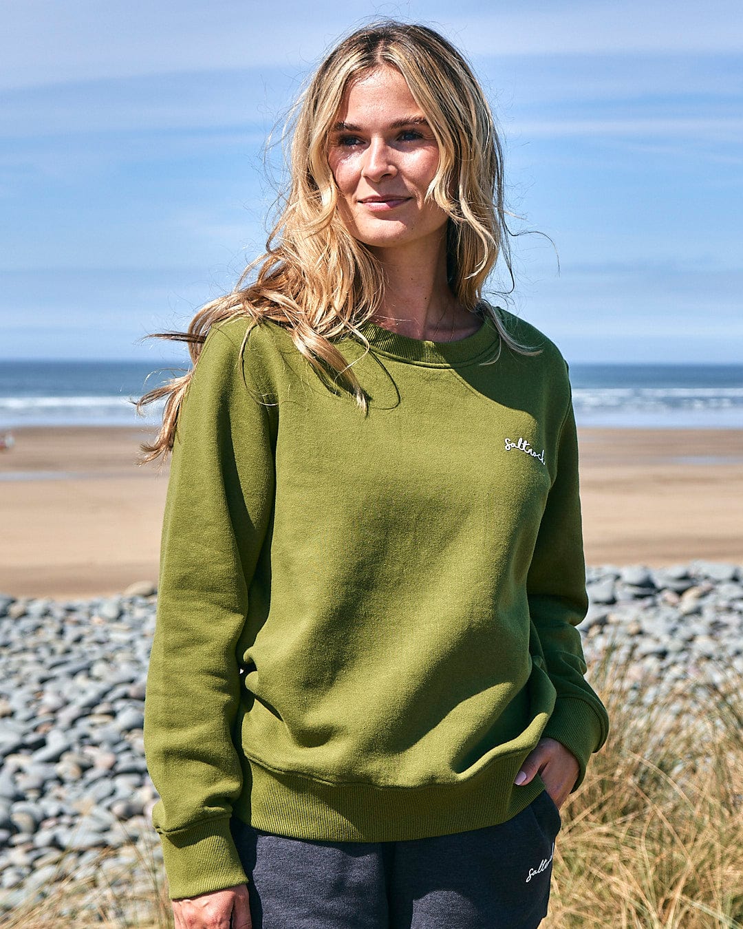 A woman is standing on the beach wearing a Saltrock Velator - Womens Long Sleeve Sweat - Dark Green.