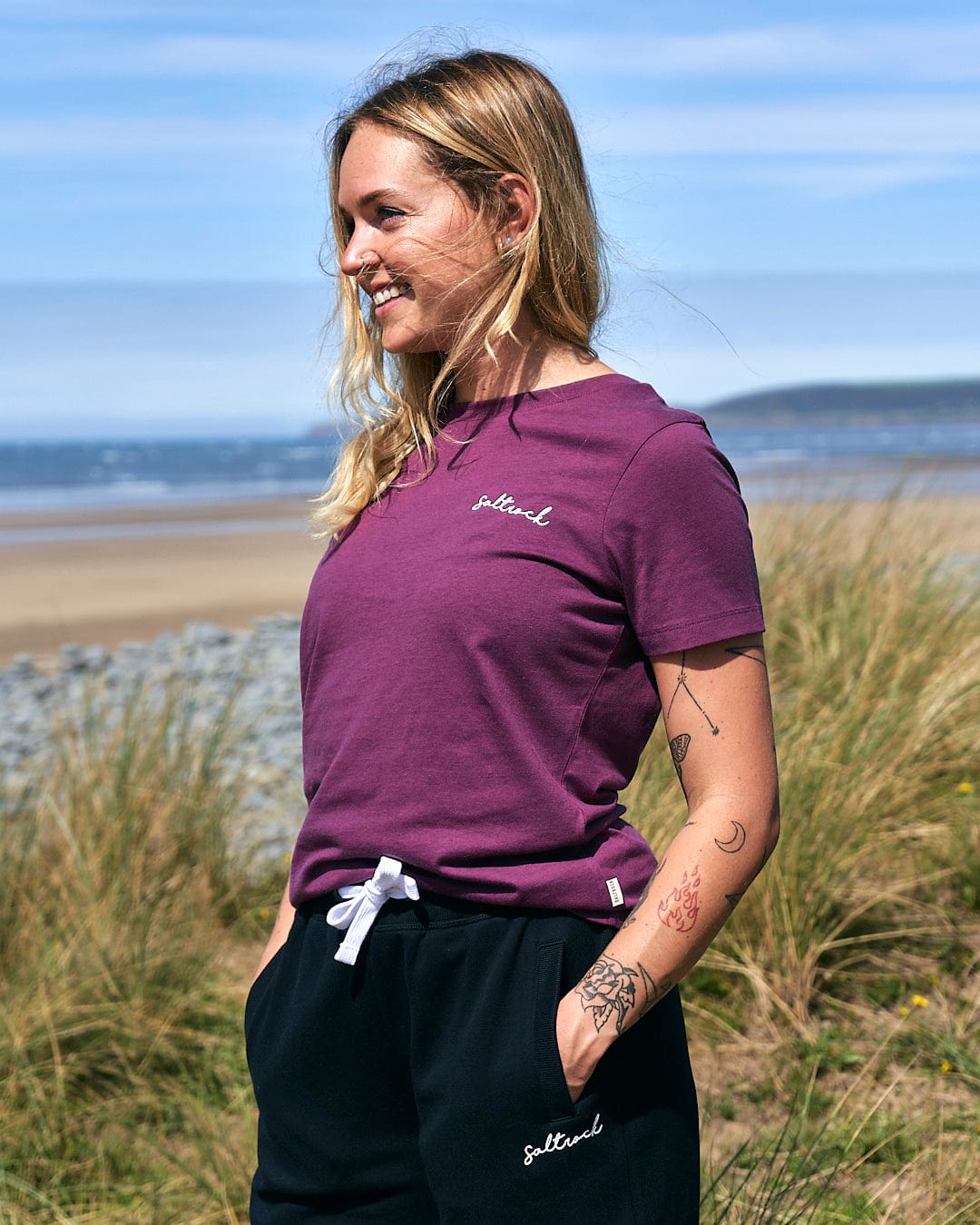 A woman wearing a Saltrock Velator - Womens Short Sleeve T-Shirt - Dark Purple and black sweatpants.