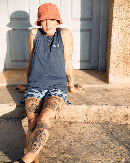 A person with tattoos wearing a Saltrock bucket hat and a Saltrock crew neckline Velator Womens Vest in Blue sits on the ground, leaning against a sunlit wall.