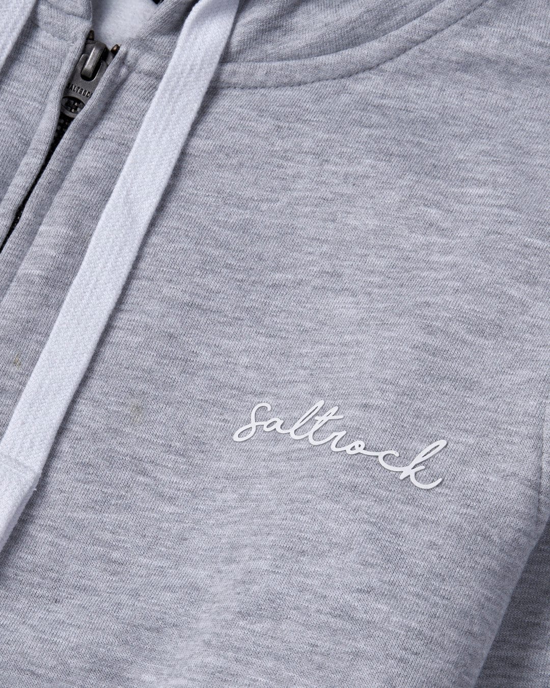 Close-up of a Saltrock Velator Women's Zip Hoodie in grey fabric with a zipper, embroidered "Saltrock" branding, and contrasting draw cords.