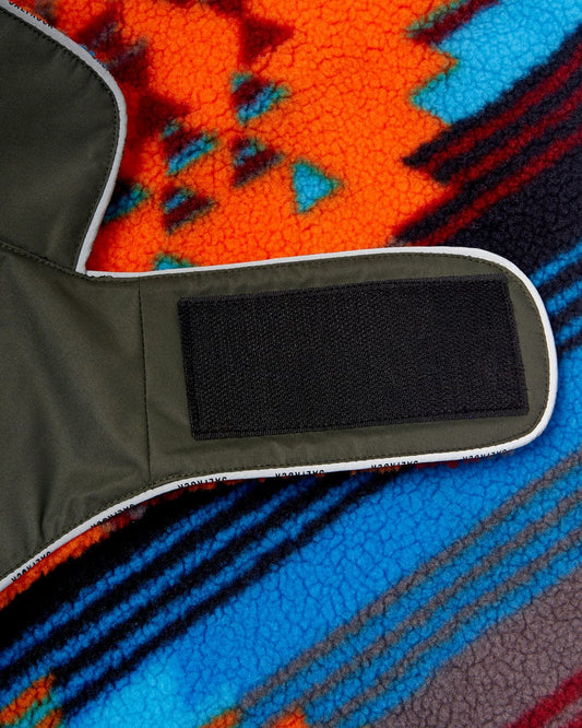 Close-up of a colorful woolen blanket with a southwestern design and a corner of a green, Water Resistant Padded Dog Jacket from Saltrock with a black velcro strap.