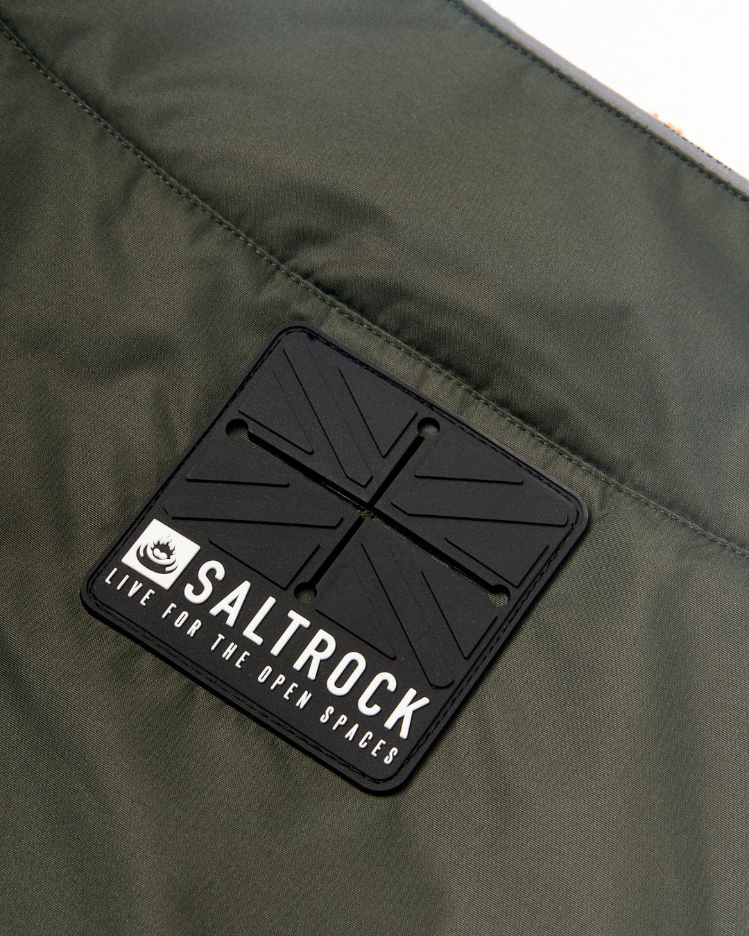Close-up view of a black Saltrock logo patch on a Waga Water Resistant Padded Dog Jacket - Green fabric background.