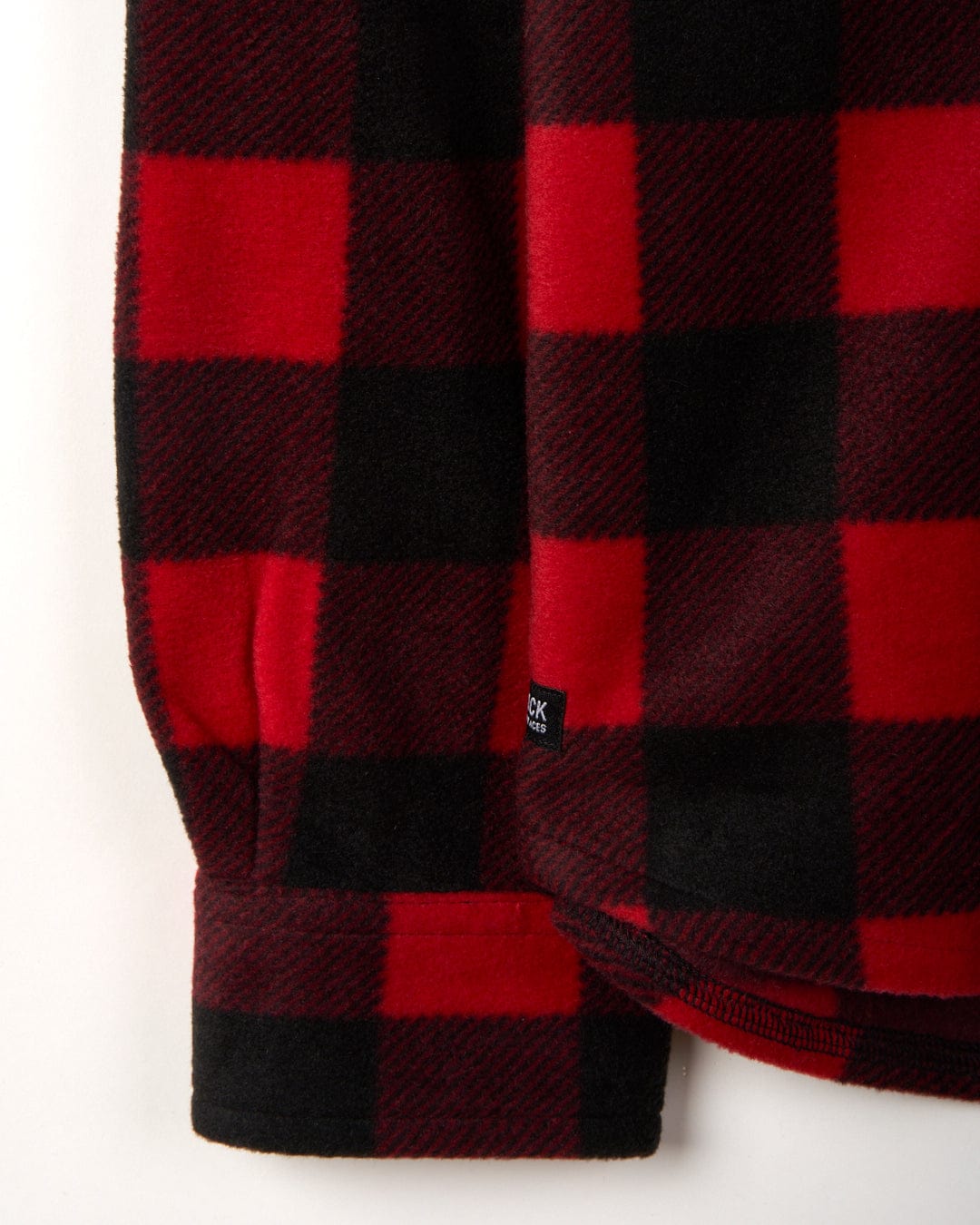 Close-up of a Saltrock Waldron - Mens Long Sleeve Shirt - Red/black check fabric with a visible clothing tag, illustrating the texture and pattern of the material.