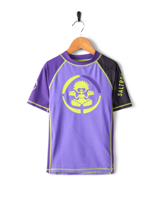 A purple and black sports jersey with a stylized yellow sun logo, crafted from Recycled Polyester, hanging on a wall-mounted coat hanger against a white background. 
Product Name: Warp Icon - Recycled Kids Short Sleeve Rashvest - Purple
Brand Name: Saltrock