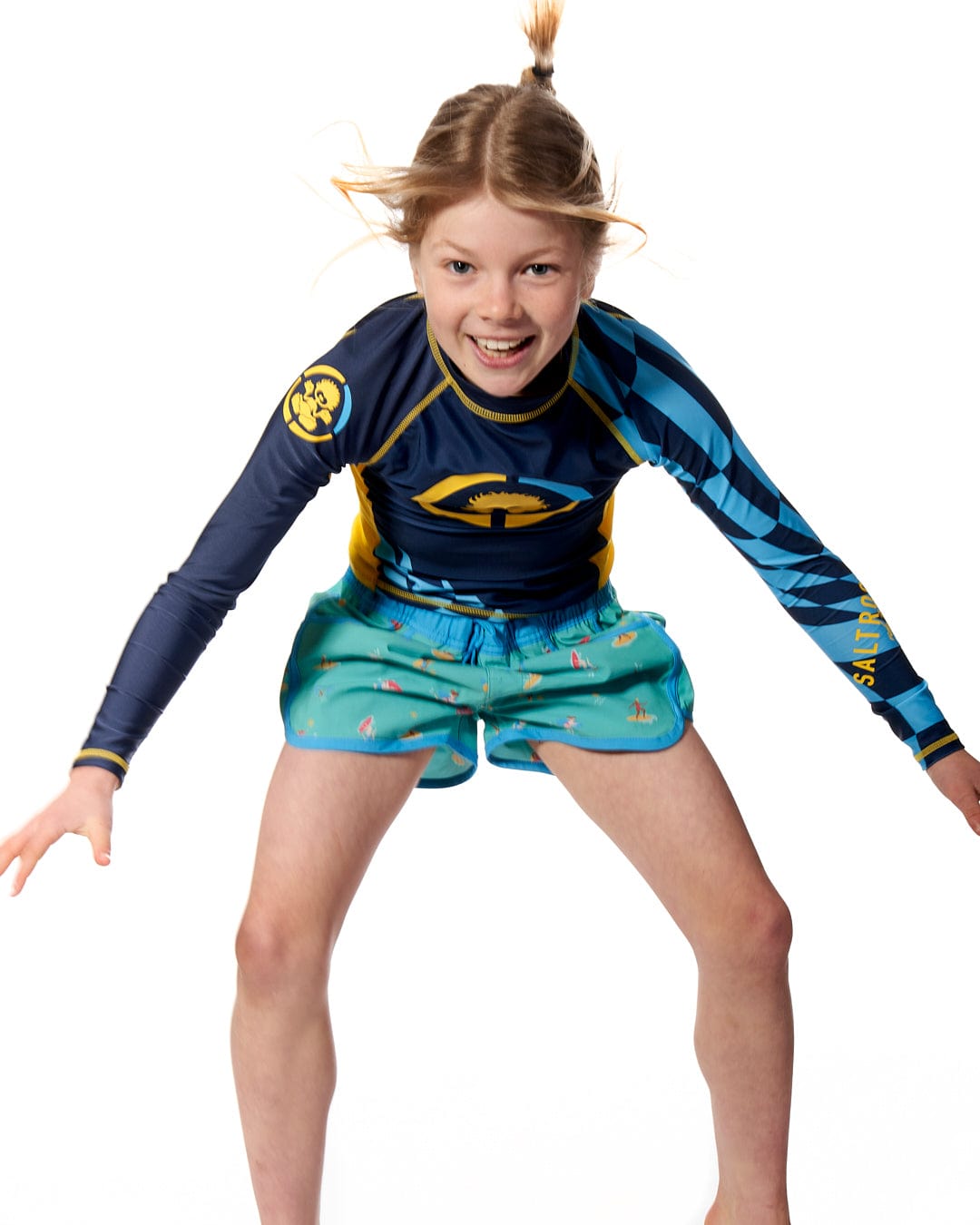 A girl wearing a Saltrock Warp - Kids Long Sleeve Rash Vest - Blue on a white background.