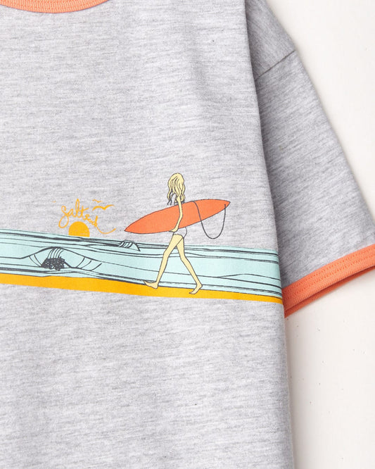 Illustration of a person with a surfboard on a Saltrock Waveline Kids Short Sleeve T-Shirt in Grey, featuring coastal motifs and sunset design with orange highlights.
