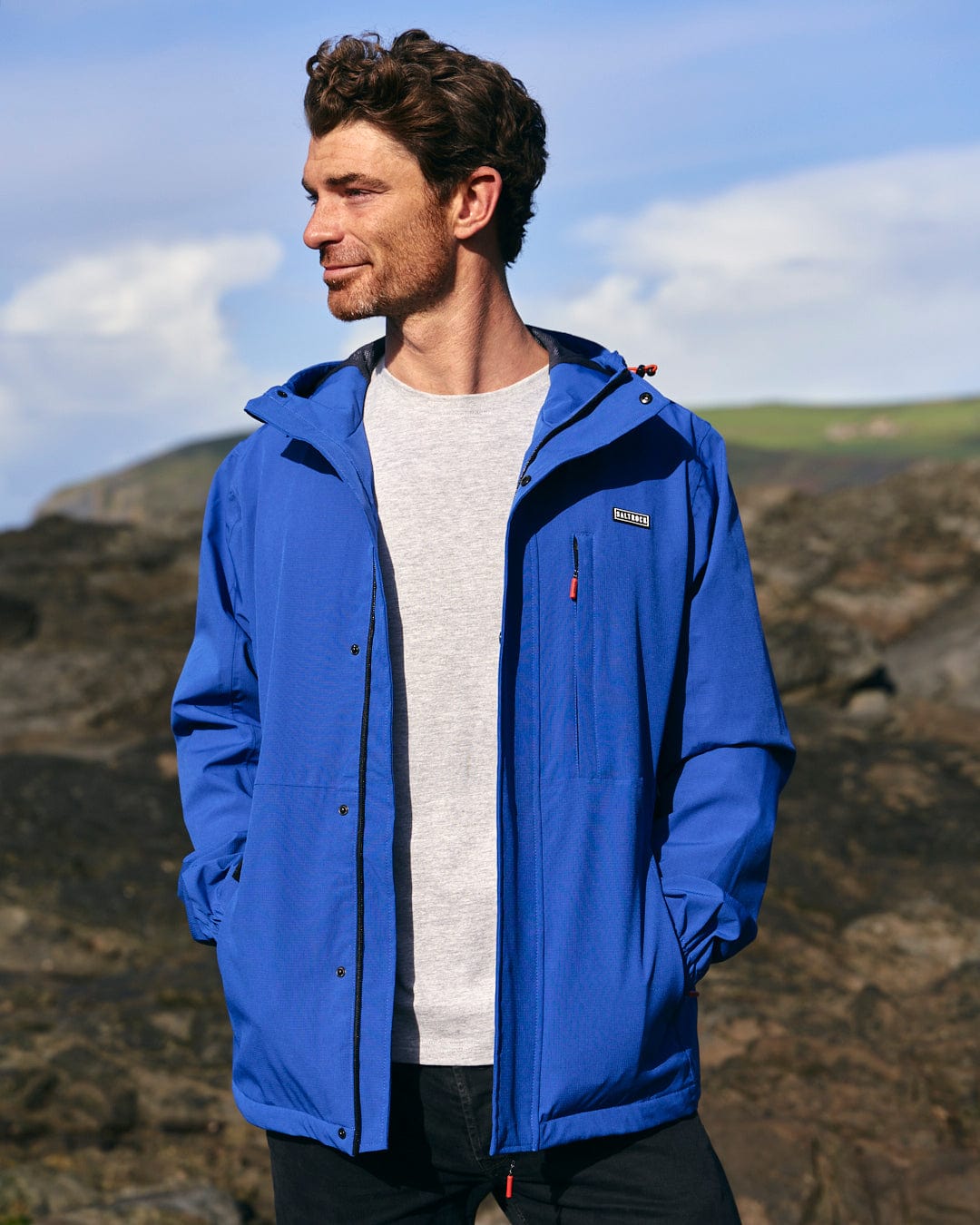 A man in a Whistler - Mens Hooded Jacket - Blue Saltrock standing on a waterproof rock.