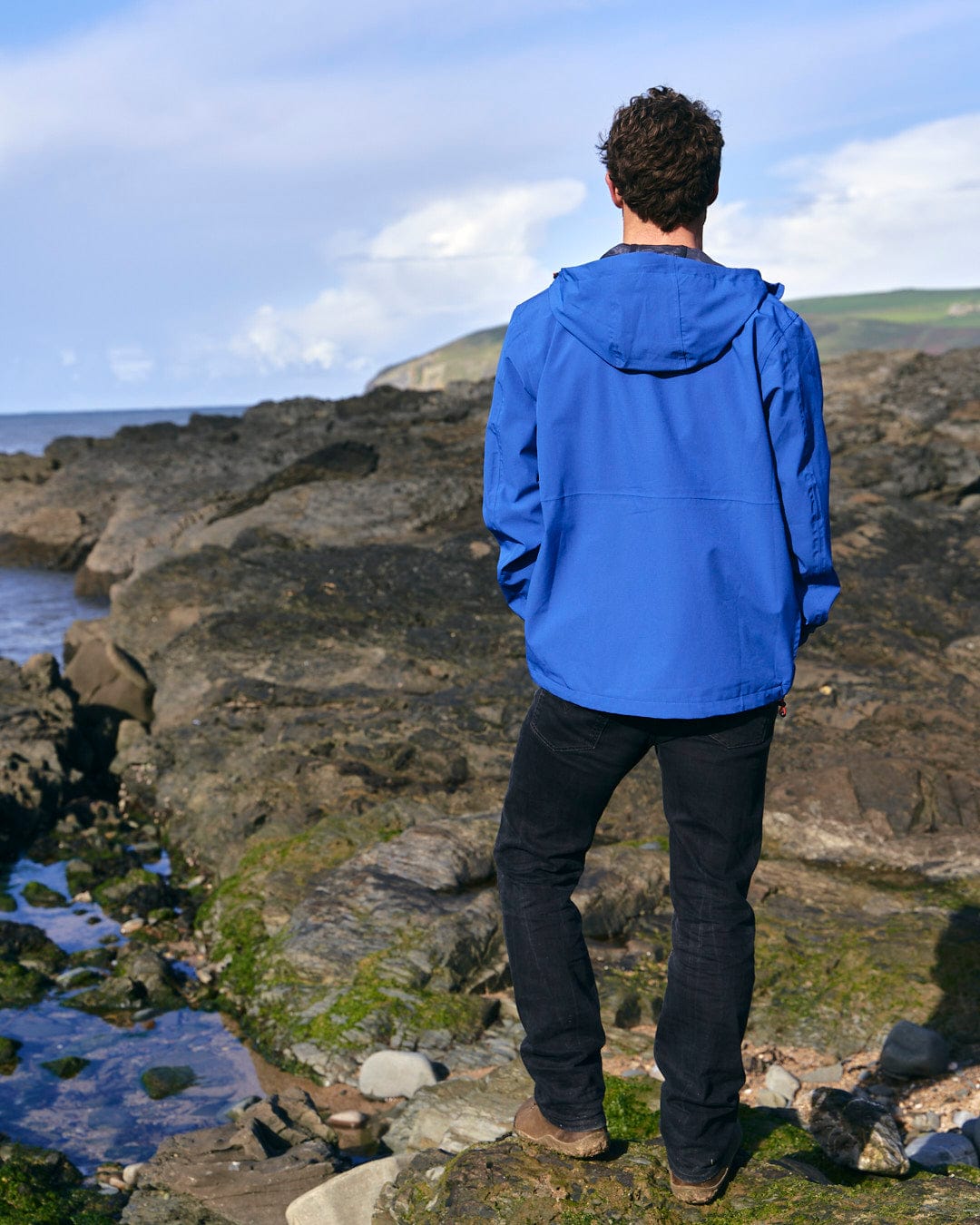 A man wearing a Saltrock Whistler - Mens Hooded Jacket - Blue standing on a rock.