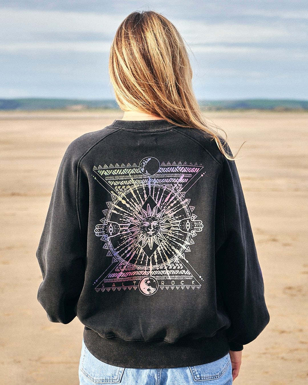 The back of a woman wearing a Saltrock Winter Solstice Gradient - Womens Sweat - Washed Black on the beach during Winter Solstice.