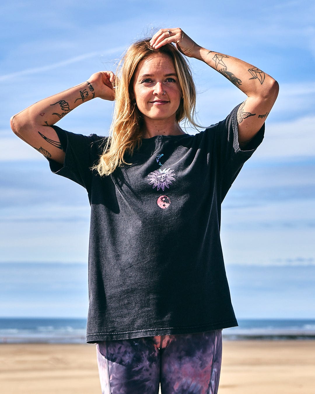 A woman wearing a Saltrock Winter Solstice Gradient - Womens Short Sleeve T-Shirt - Washed Black standing on the beach.