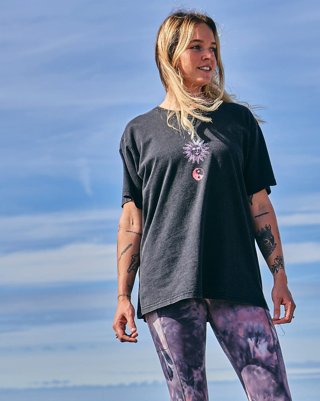 A woman wearing a Winter Solstice Gradient - Womens Short Sleeve T-Shirt - Washed Black by Saltrock and purple leggings.