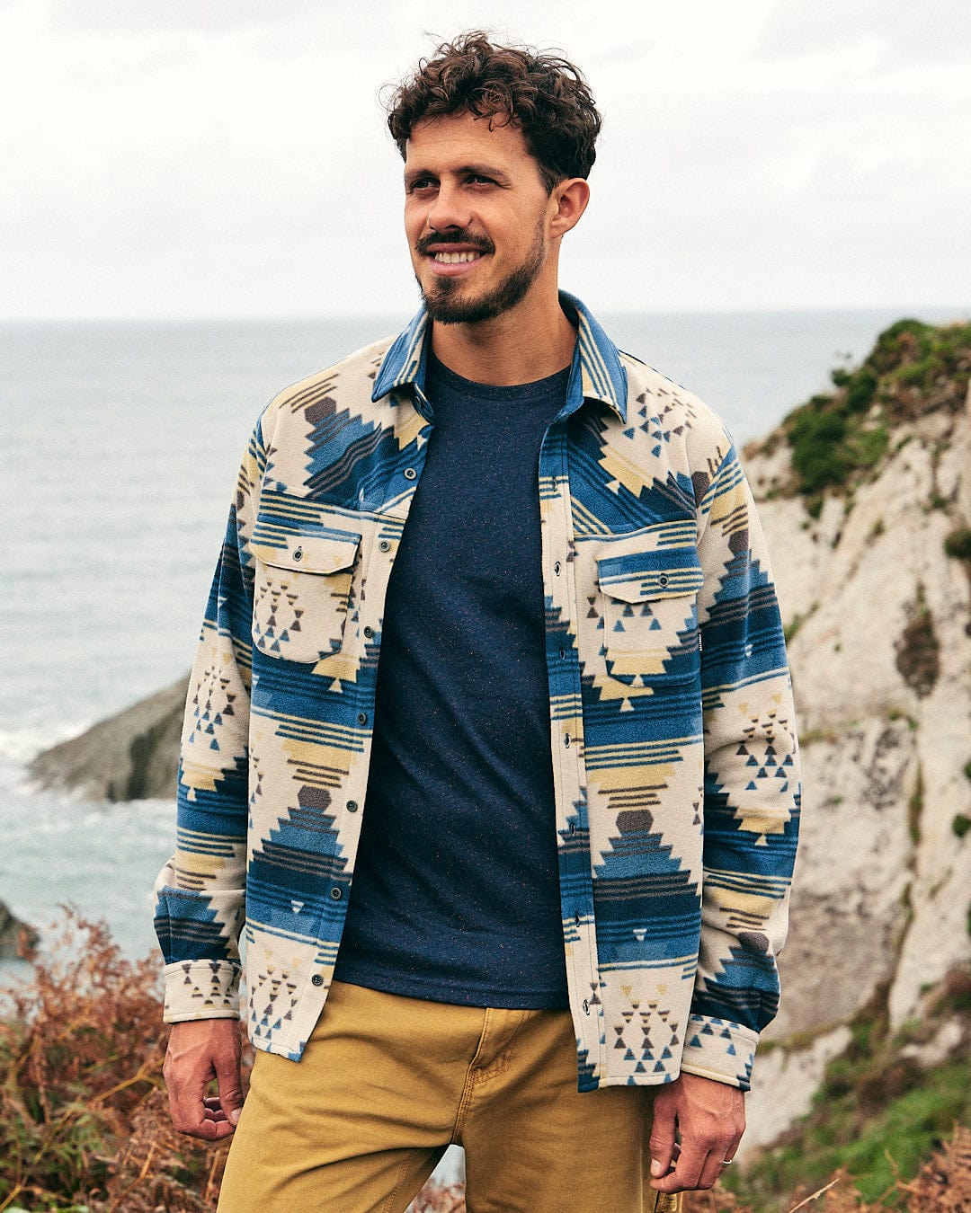 A man wearing a Wolfe - Mens Aztec Fleece Shirt - Blue Saltrock shirt enjoying the warmth of the ocean breeze.