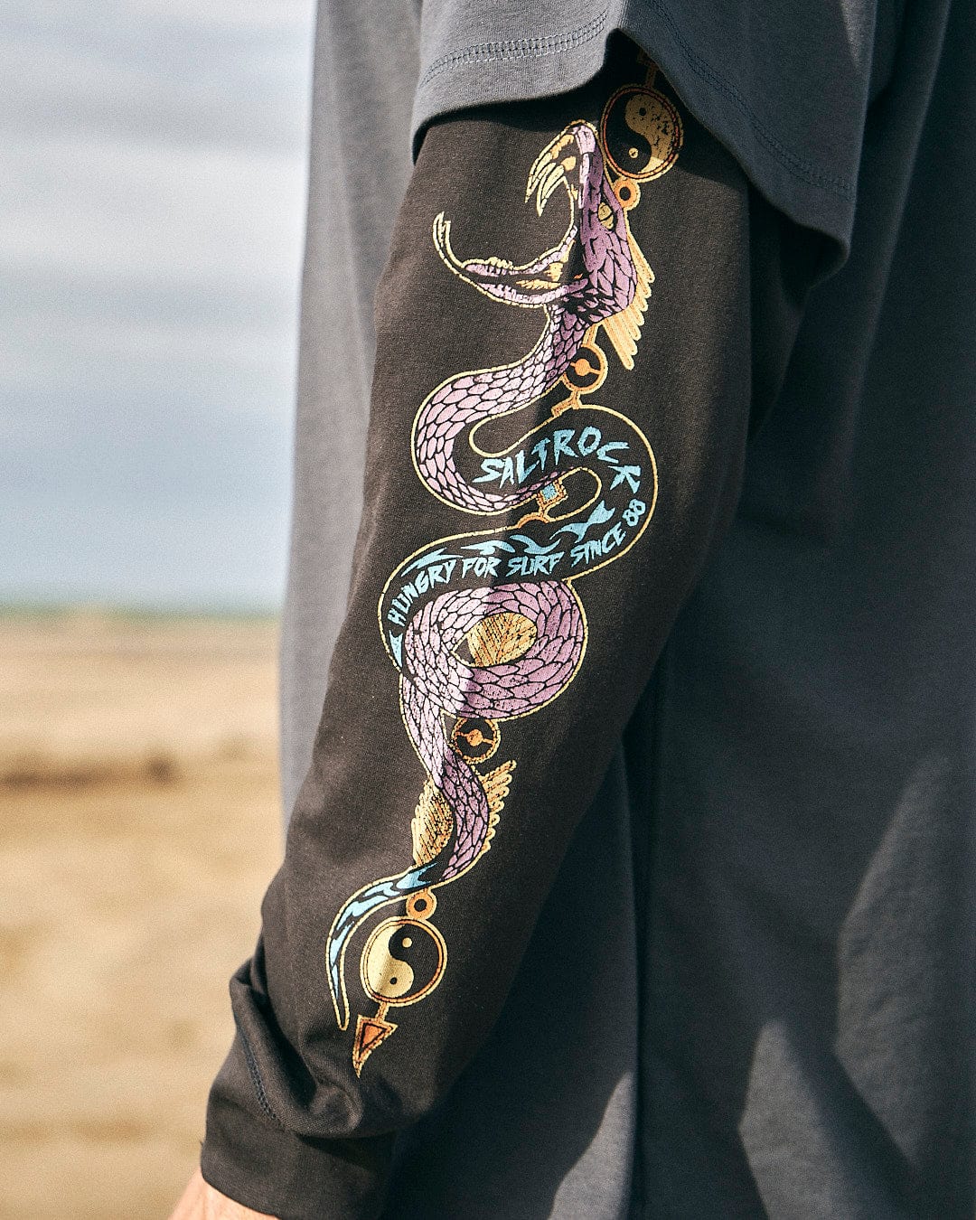 A man wearing a Saltrock Wolfscale - Mens Double Layer Long Sleeve T-Shirt in Black with a dragon on it.
