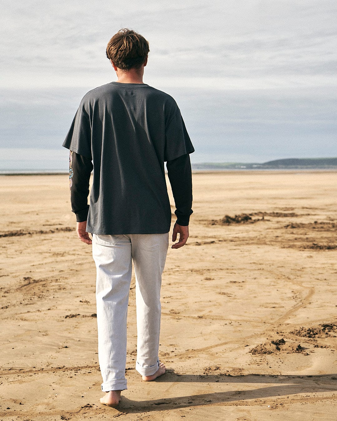 A man walking on a beach wearing a Saltrock - Wolfscale Mens Double Layer Long Sleeve T-Shirt in Black.