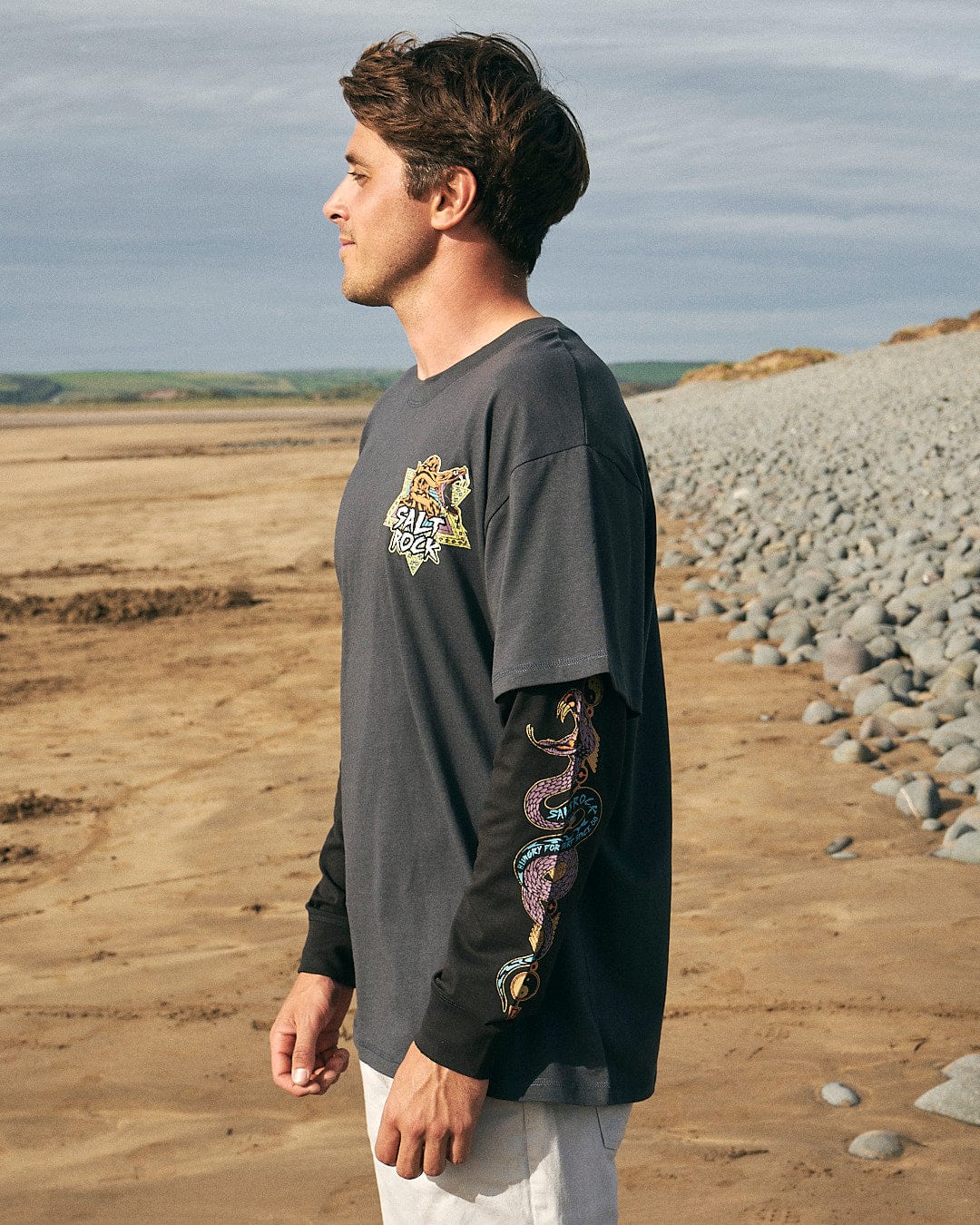 A man standing on a beach wearing a Saltrock - Wolfscale - Mens Double Layer Long Sleeve T-Shirt - Black.