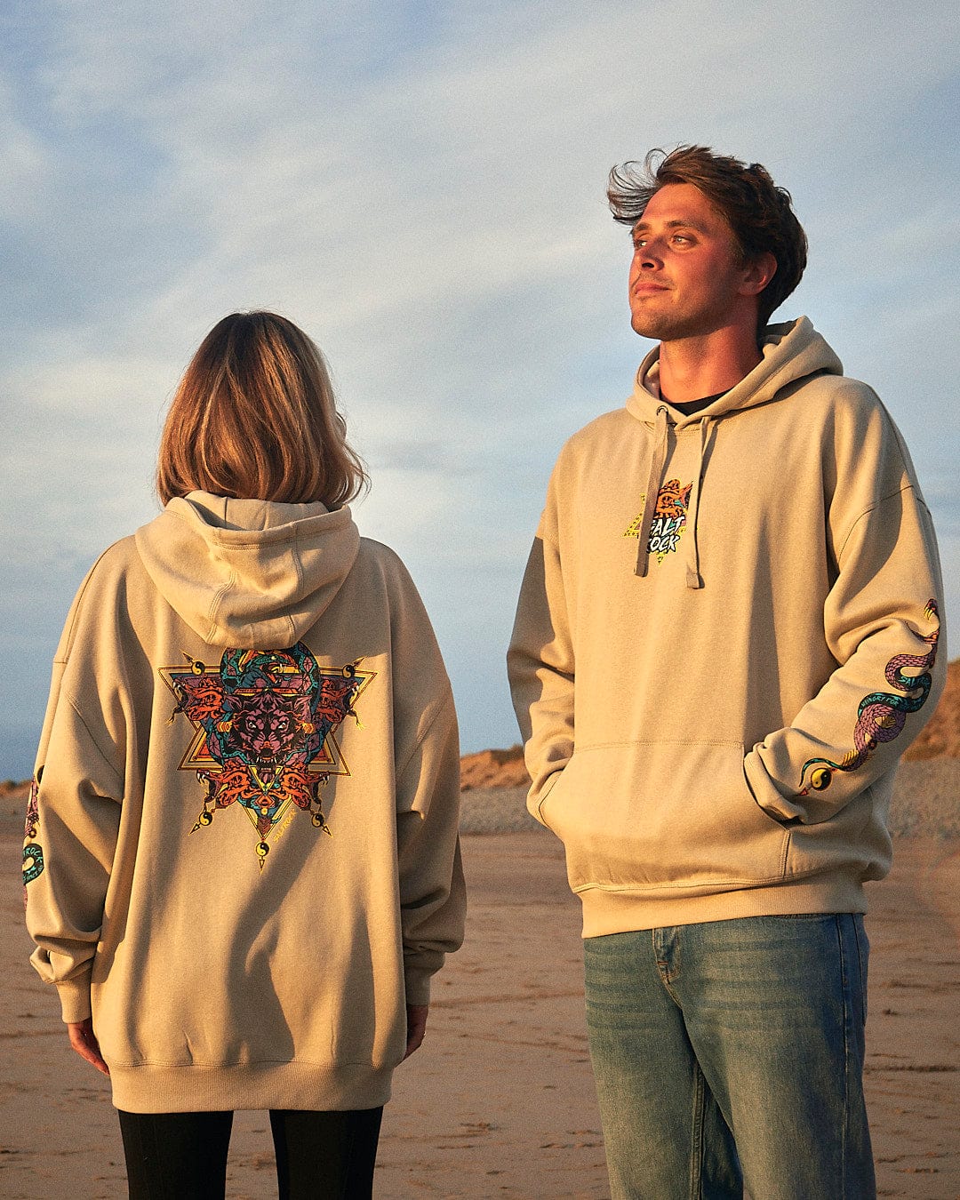 A man and woman standing on the beach wearing a Saltrock Wolfscale - Pop Hoodie - Beige.