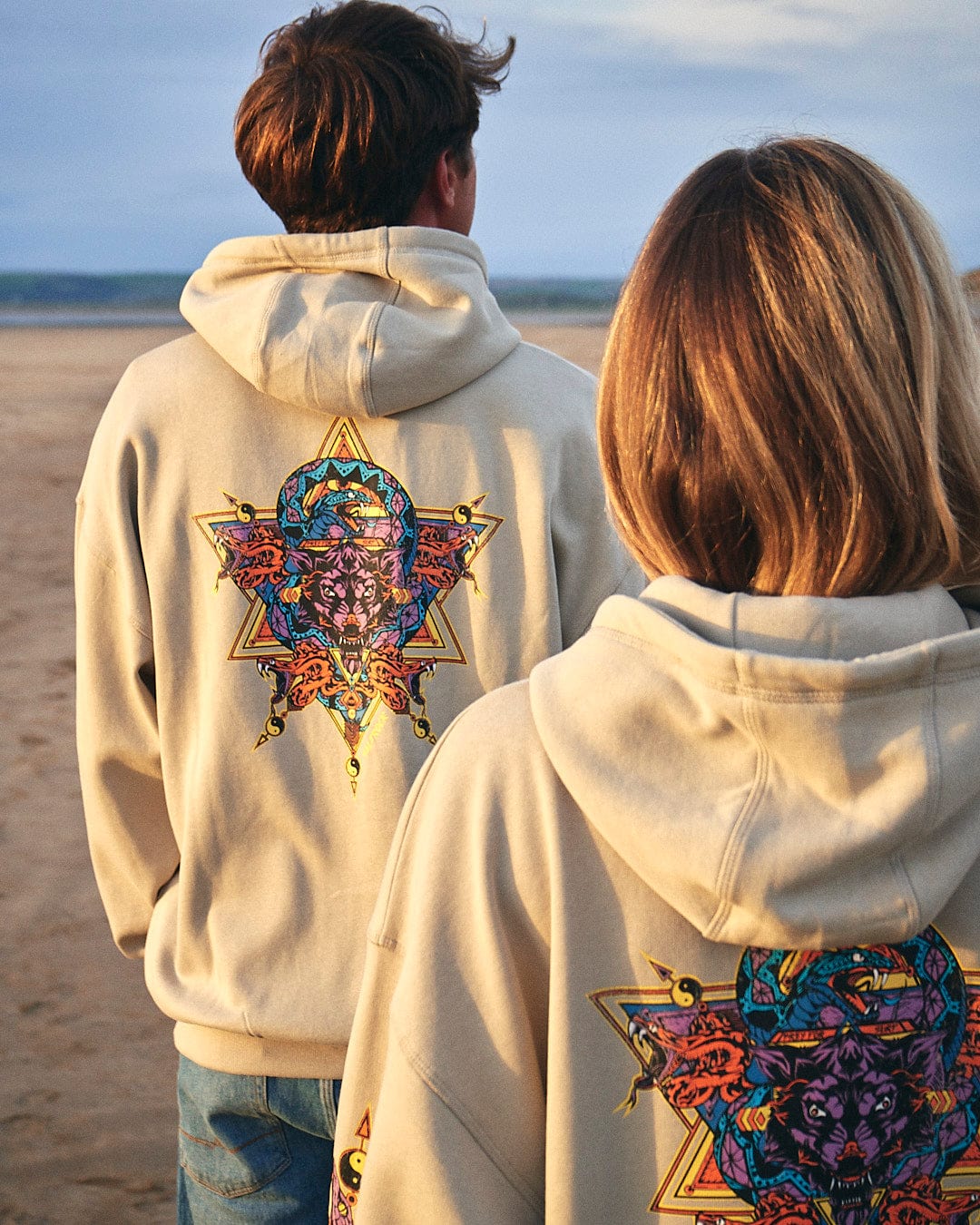 Two people standing on the beach wearing Wolfscale - Pop Hoodie - Beige hoodies featuring Saltrock branding.