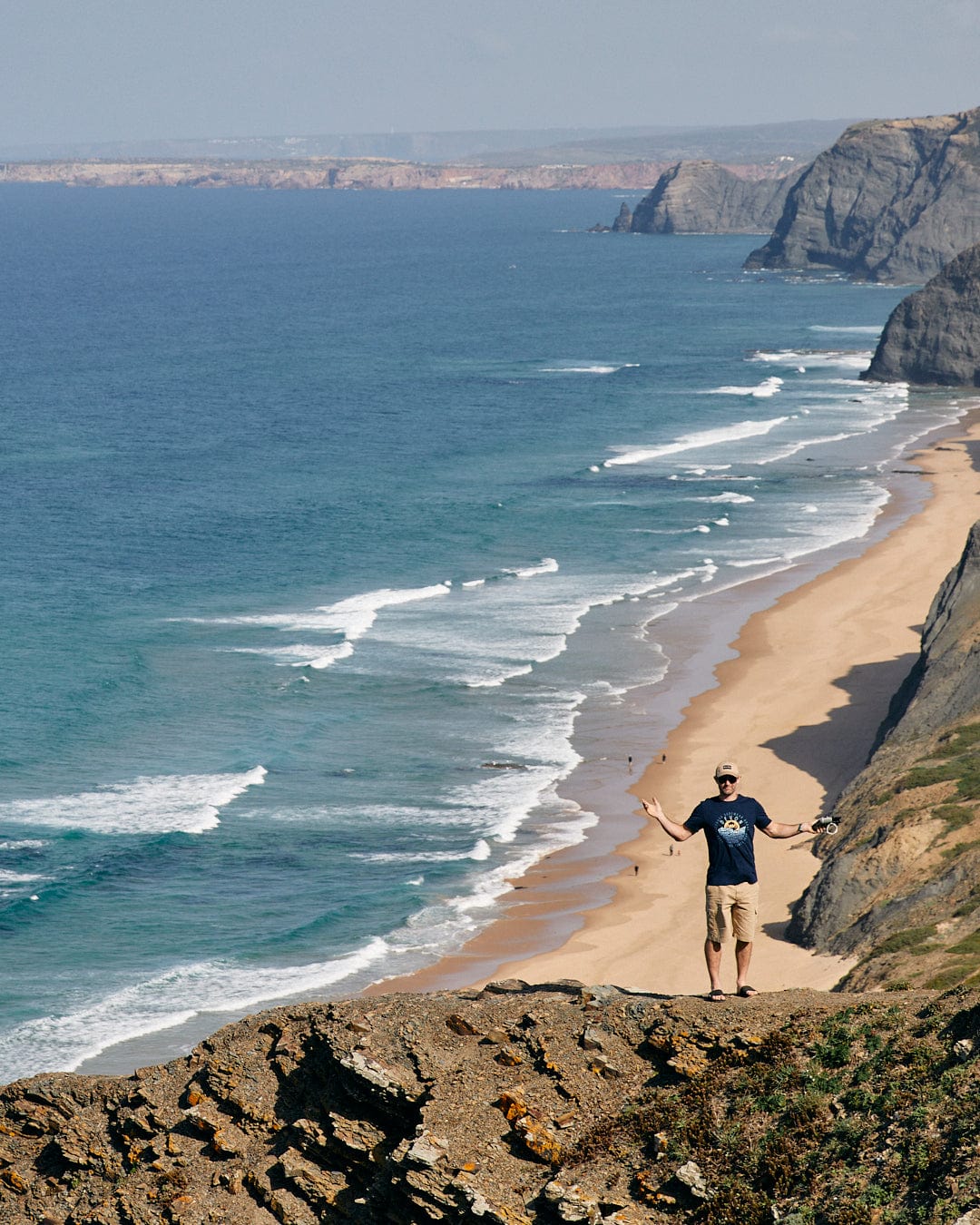 A man is flying a kite over the ocean, enjoying the Layers Devon - Mens Short Sleeve T-Shirt - Blue with Saltrock branding on his peached soft material.