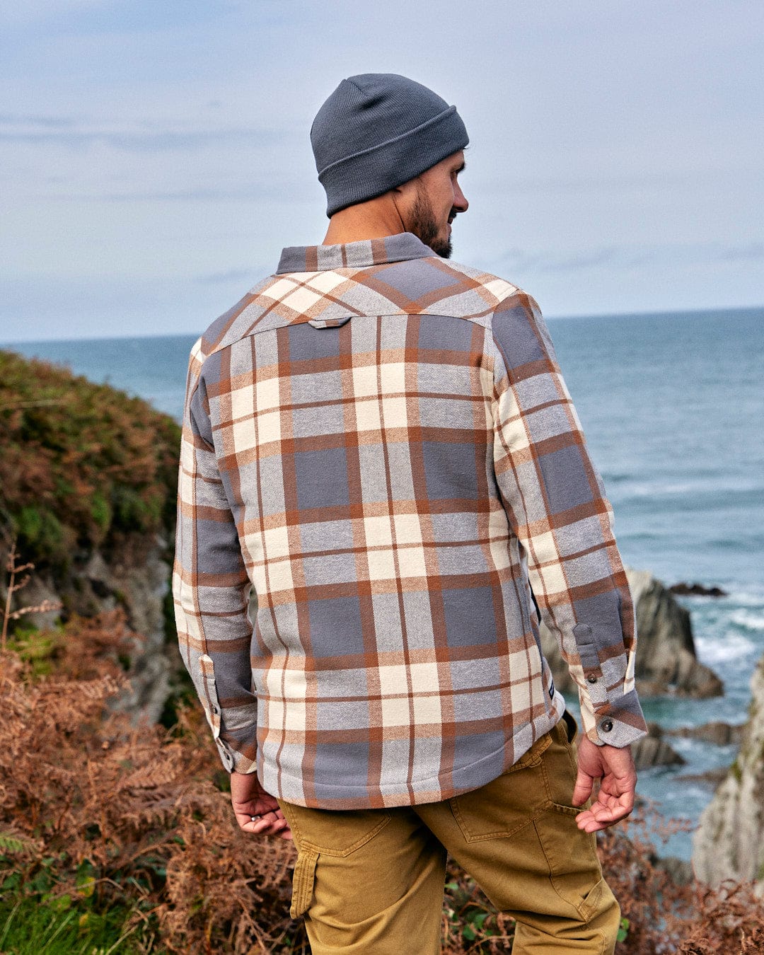 A stylish man wearing a Saltrock Woody - Mens Sherpa Lined Shacket - Brown looking at the ocean.