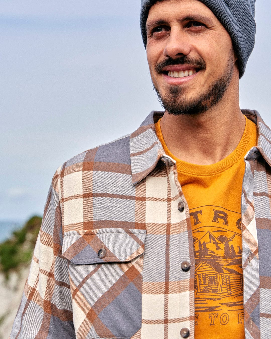 A man wearing a plaid shirt and a beanie with Saltrock's Woody - Mens Sherpa Lined Shacket - Brown.