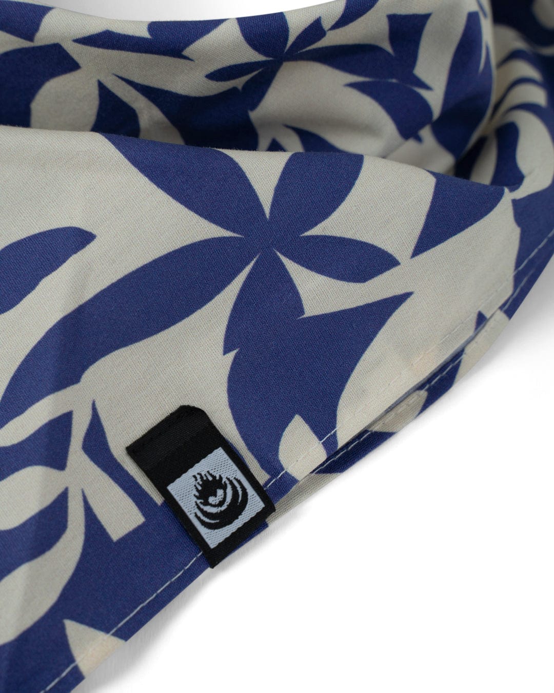 Close-up of Saltrock's Balance - Bandana - Blue, made from 100% cotton with blue and white floral patterns and a black and white tag featuring an eye design sewn into the seam.