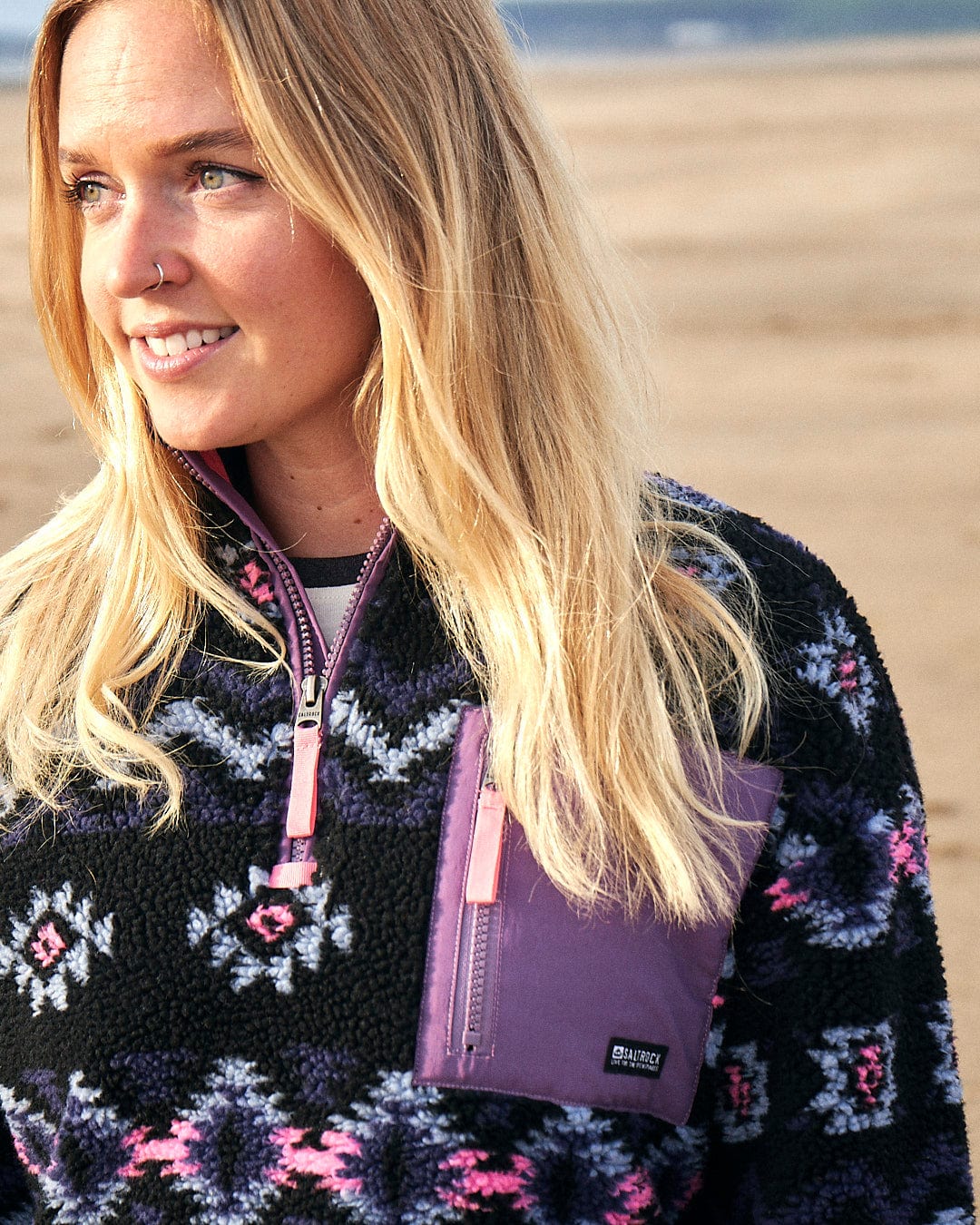 A woman is standing on the beach wearing a Saltrock - Zella Womens 1/4 Neck Fleece - Black sweater.