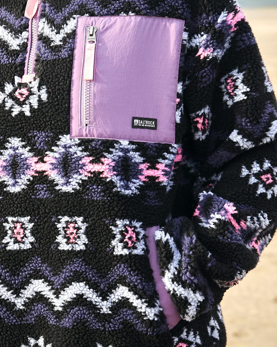 A woman wearing a Saltrock Zella - Womens 1/4 Neck Fleece - Black aztec pullover on the beach.