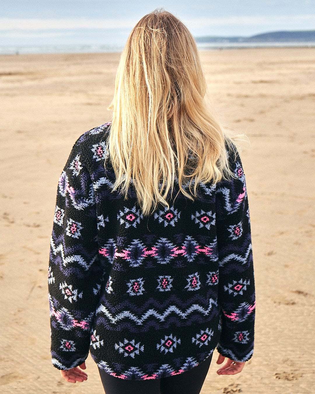 A woman wearing a black and white Zella - Womens 1/4 Neck Fleece by Saltrock walking on the beach.