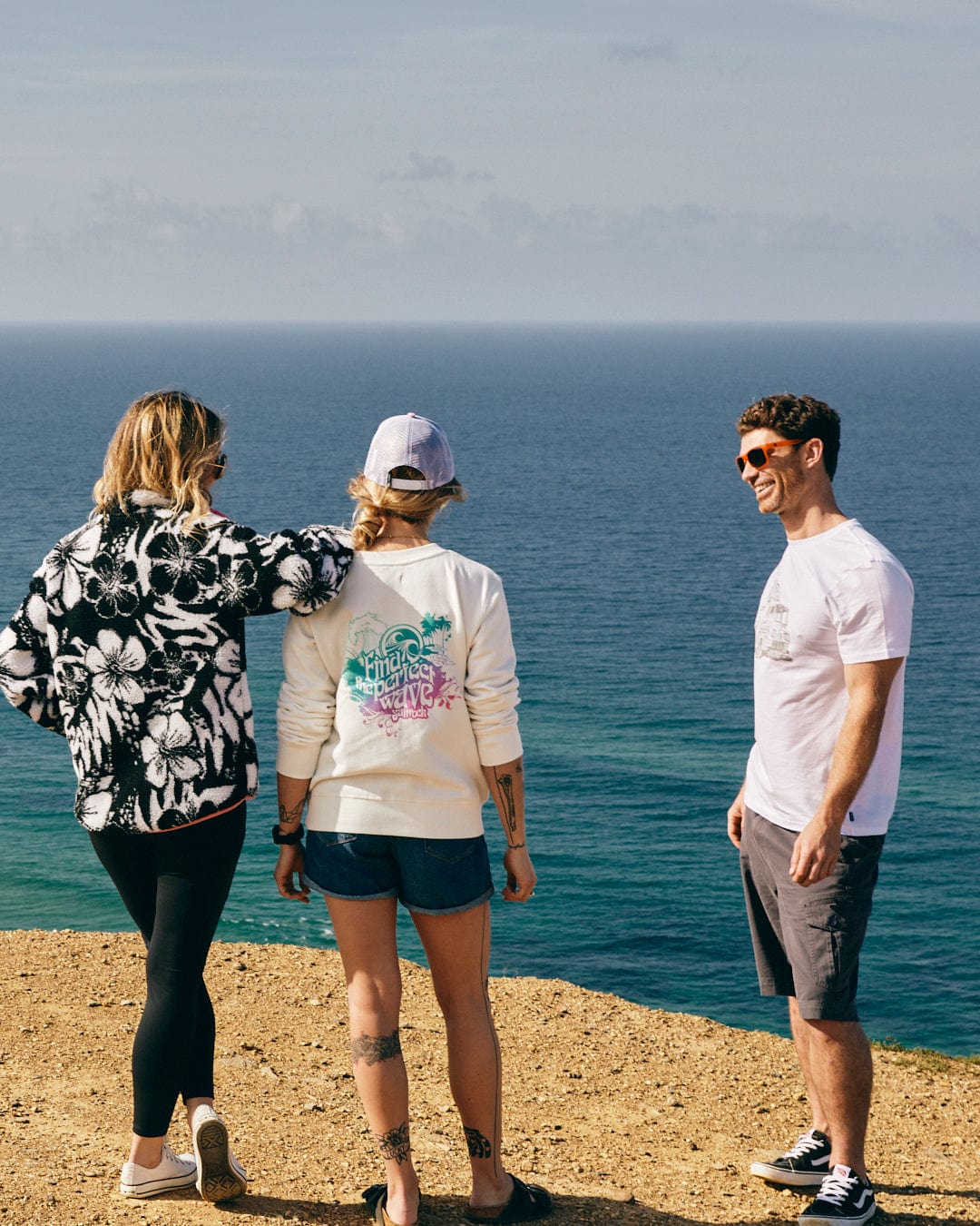 A group of people standing on a cliff overlooking the ocean wearing Saltrock's Zella Hibiscus - Womens 1/4 Neck Fleece - Black Floral.