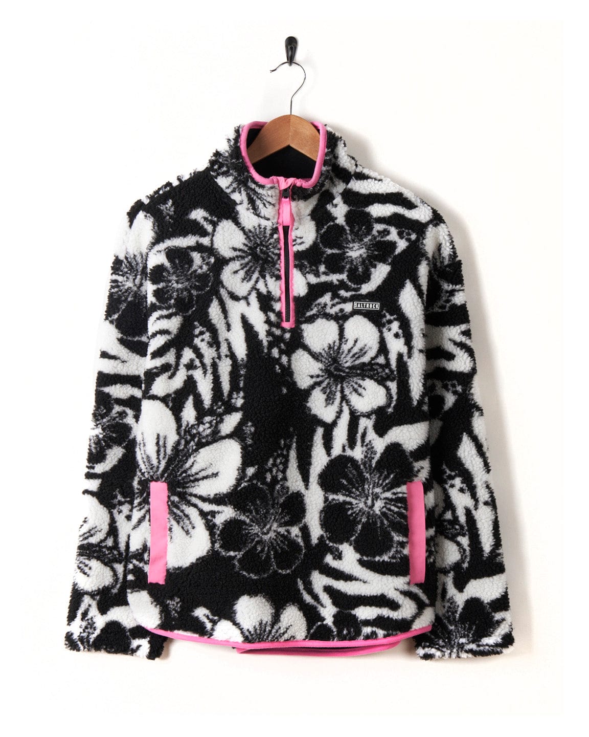 A black and pink Zella Hibiscus - Womens 1/4 Neck Fleece - Black Floral sweatshirt made of 100% polyester fleece material, hanging on a hanger. (Brand: Saltrock)