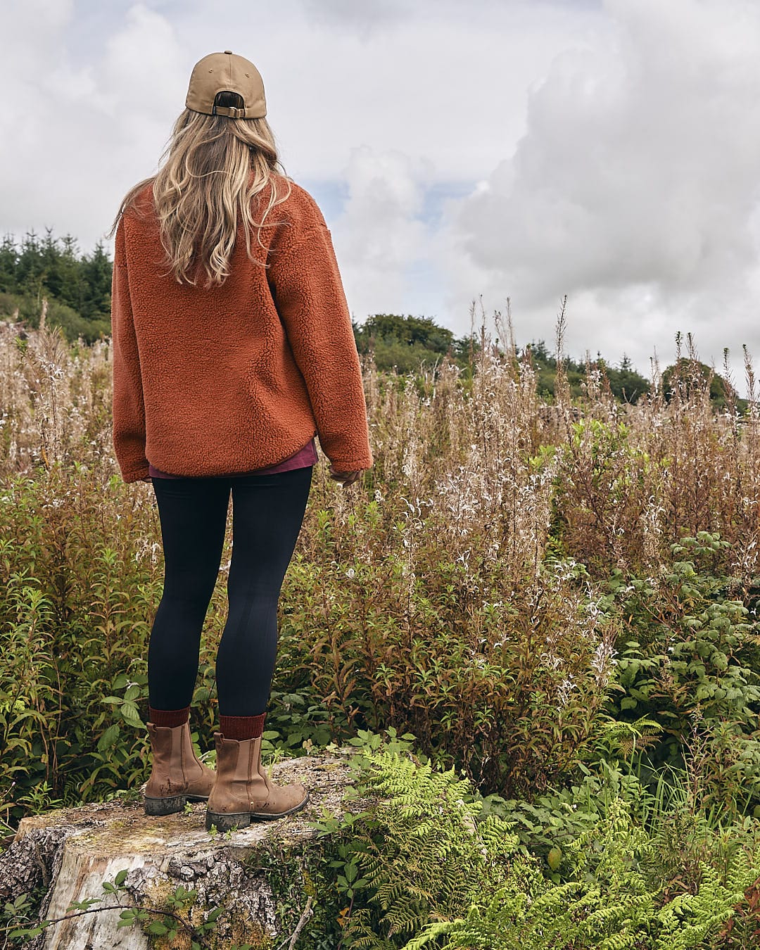 A woman standing on a rock in a field wearing the Saltrock Zella Solid - Womens Borg Fleece - Burnt Orange.