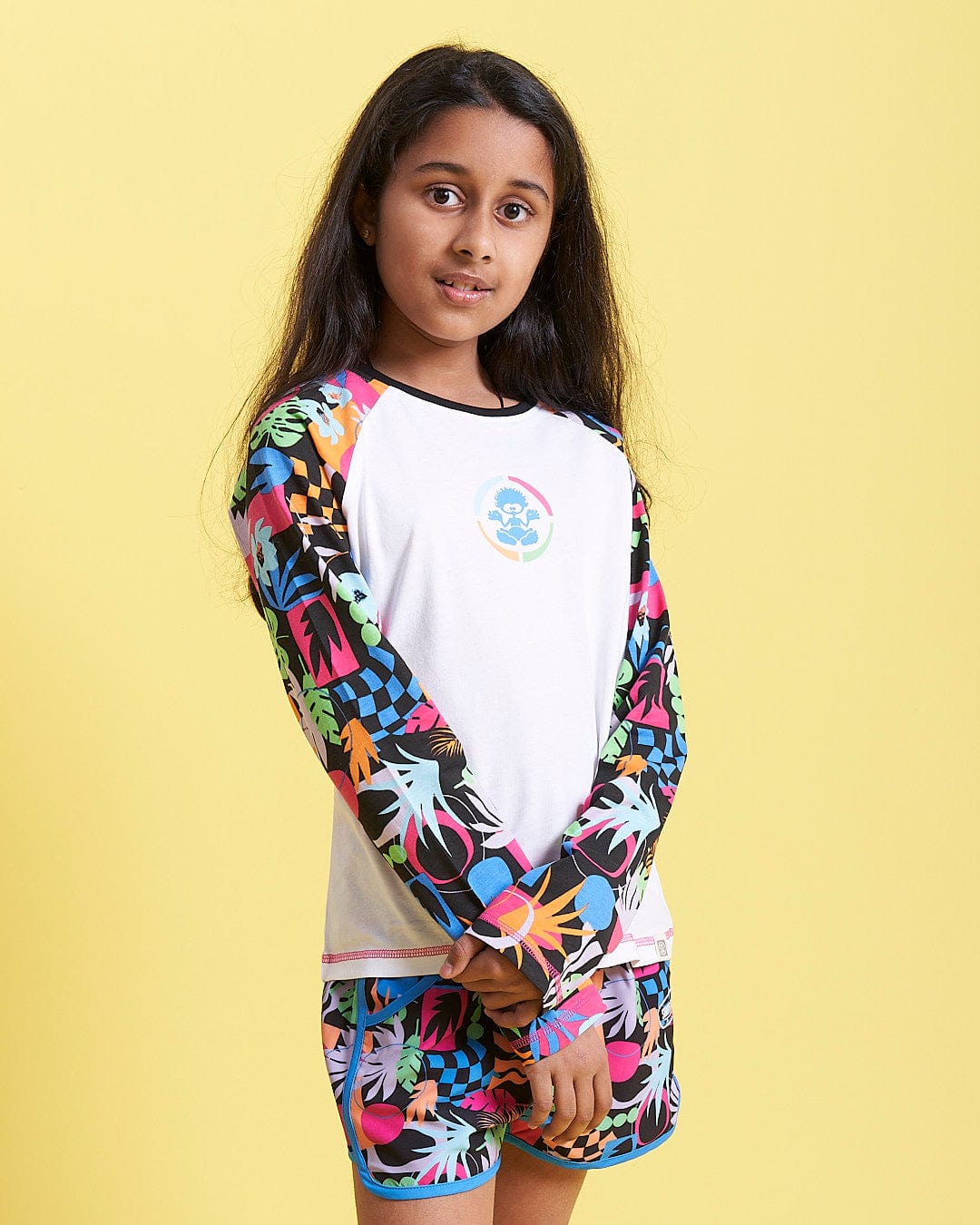 A young girl wearing a Saltrock Zephyr Tok - Kids Raglan Long Sleeve T-Shirt - White and shorts.