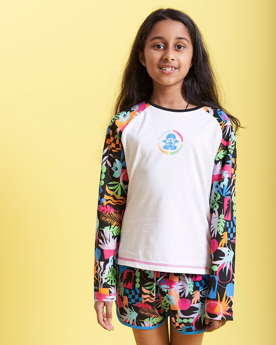 A young girl wearing a Saltrock Zephyr Tok - Kids Raglan Long Sleeve T-Shirt - White and shorts.
