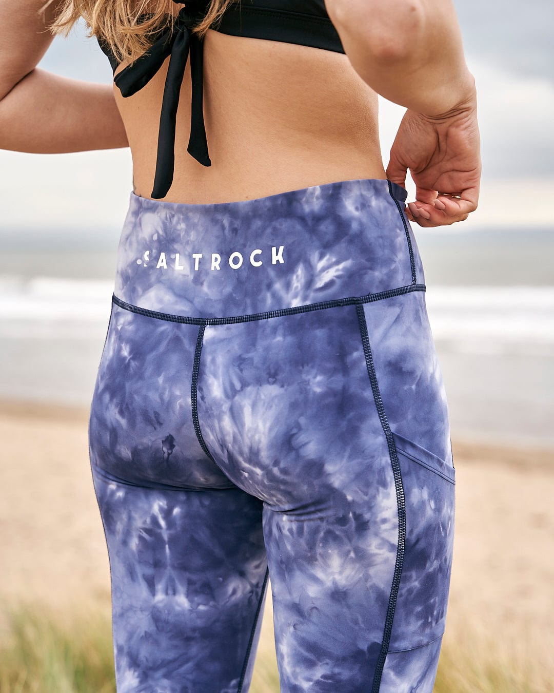 A woman wearing Saltrock Ahimsa womens leggings in blue tie dye with stretch material on the beach.