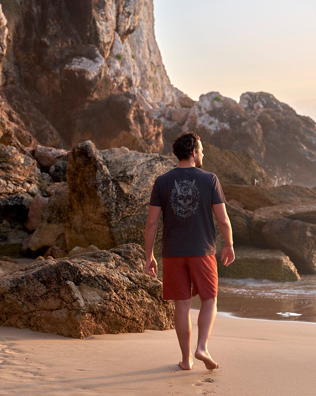 a man walking on the beach with a Saltrock Amphibian II - Mens Boardshort - Red.