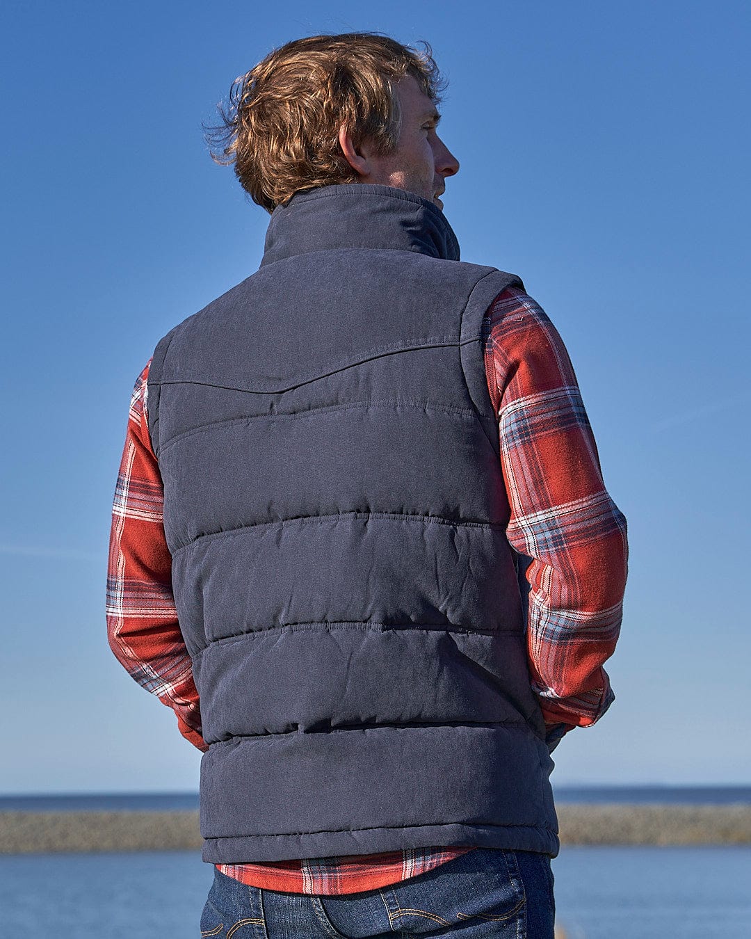 A man wearing a Saltrock Bardsey - Mens Gilet - Blue looking at the water.
