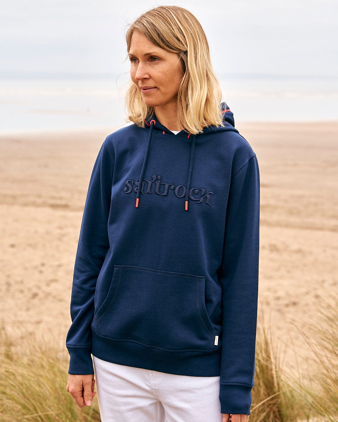 a woman wearing a Saltrock Celeste Pipe - Womens Pop Hoodie - Blue standing on the beach.