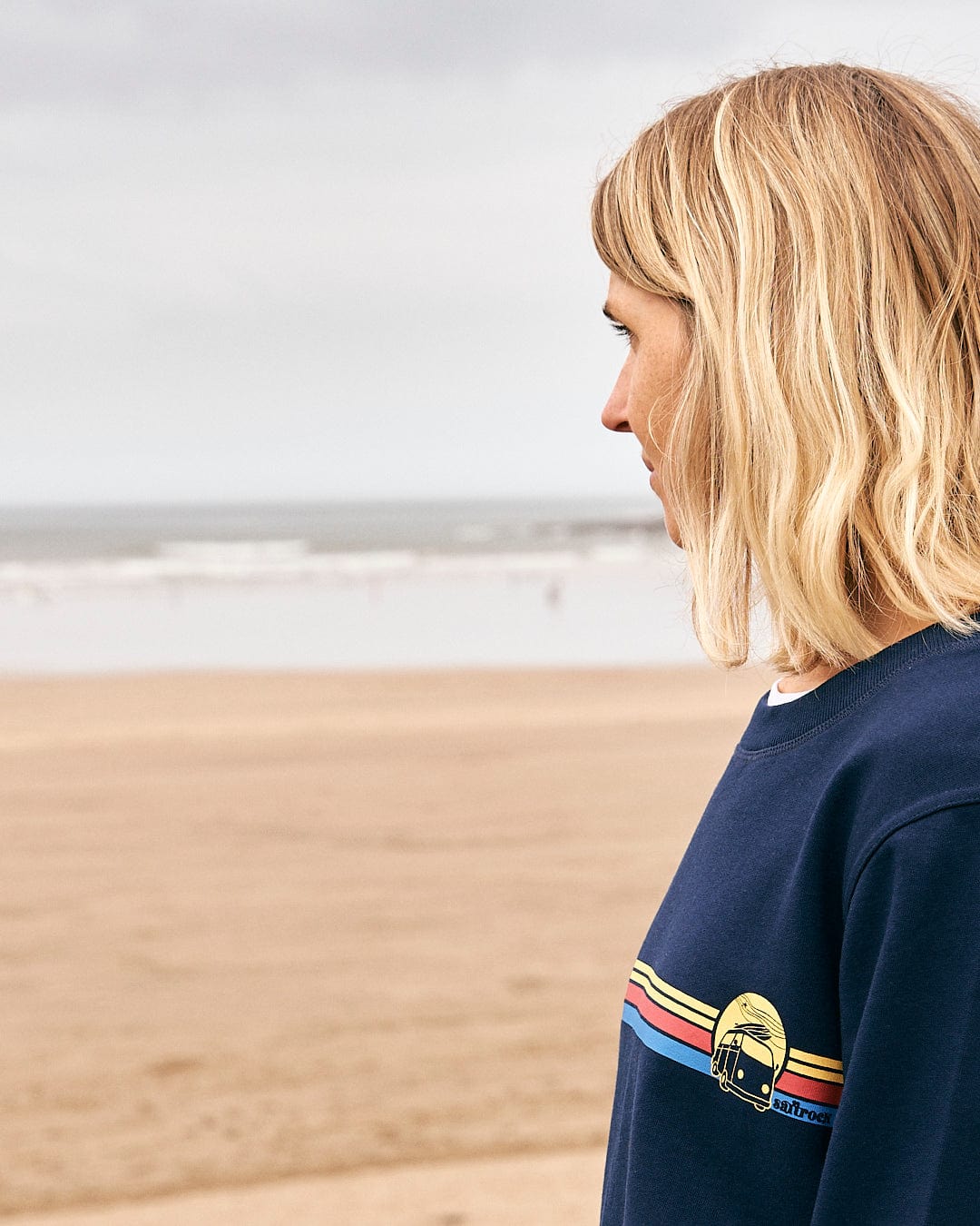 A woman standing on the beach wearing a Saltrock Celeste Stripe - Womens Crew Sweat - Blue.