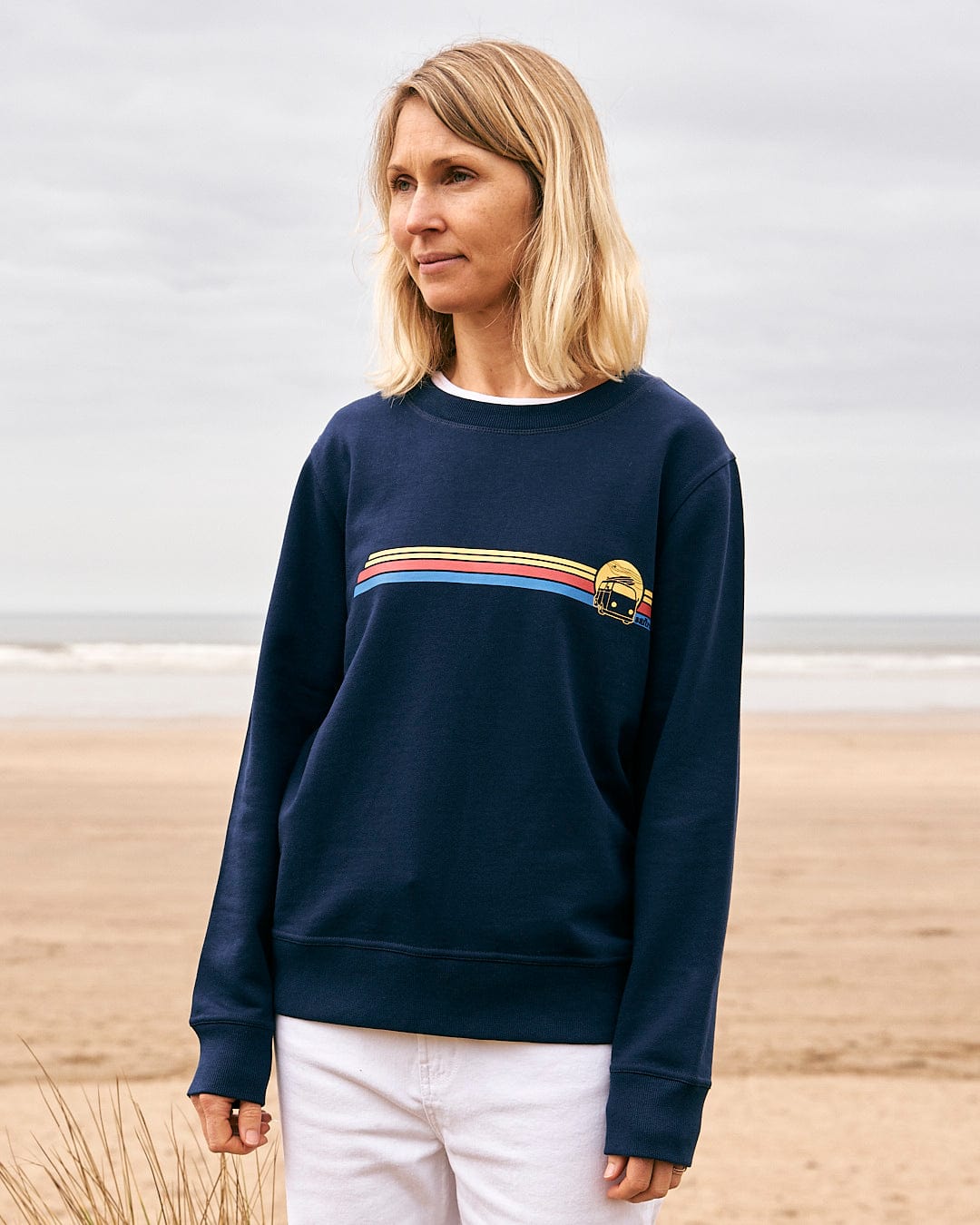 A woman standing on the beach wearing a Saltrock Celeste Stripe - Womens Crew Sweat - Blue.
