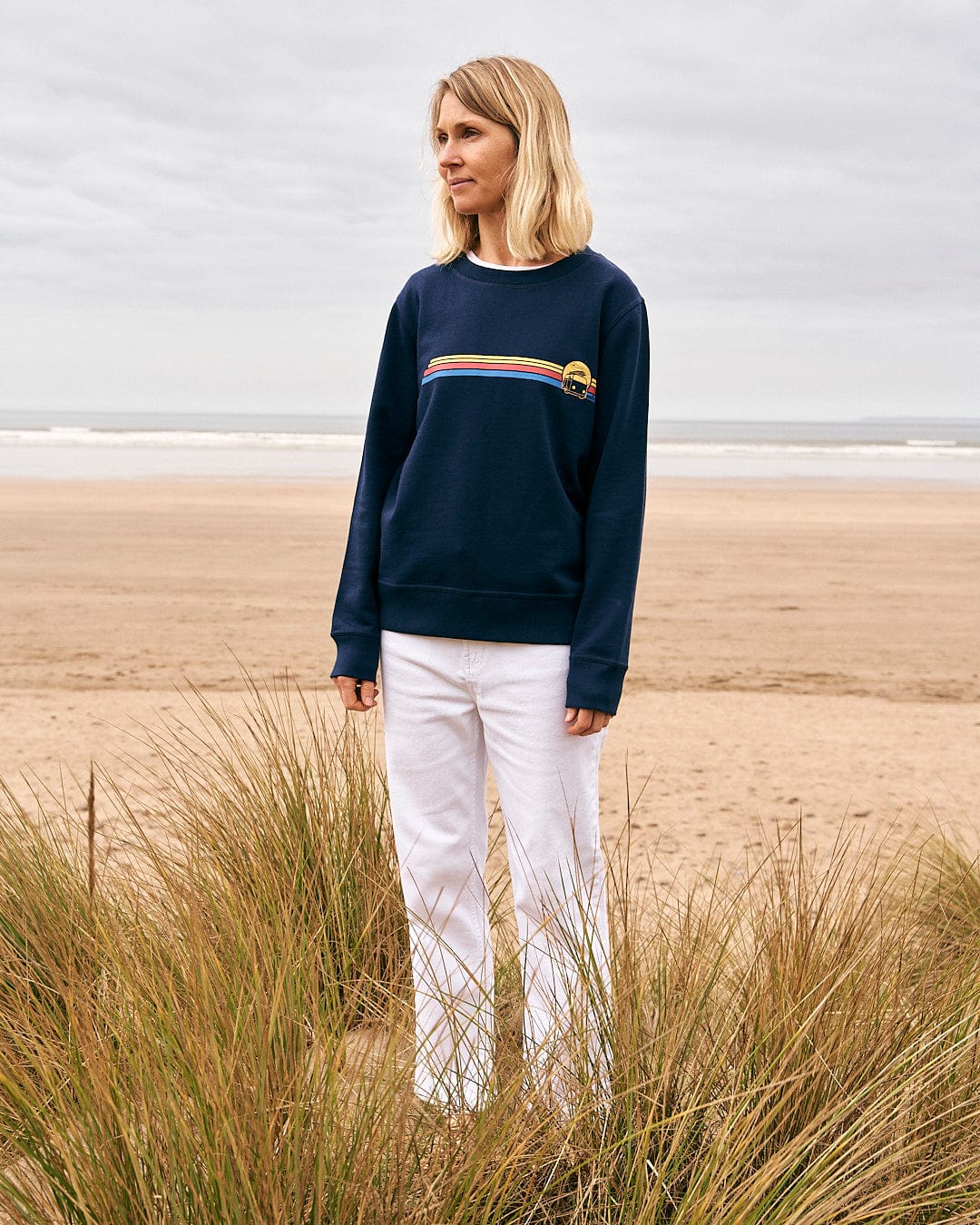 A woman standing on the beach wearing a Saltrock sweatshirt with the Celeste Stripe - Womens Crew Sweat - Blue.