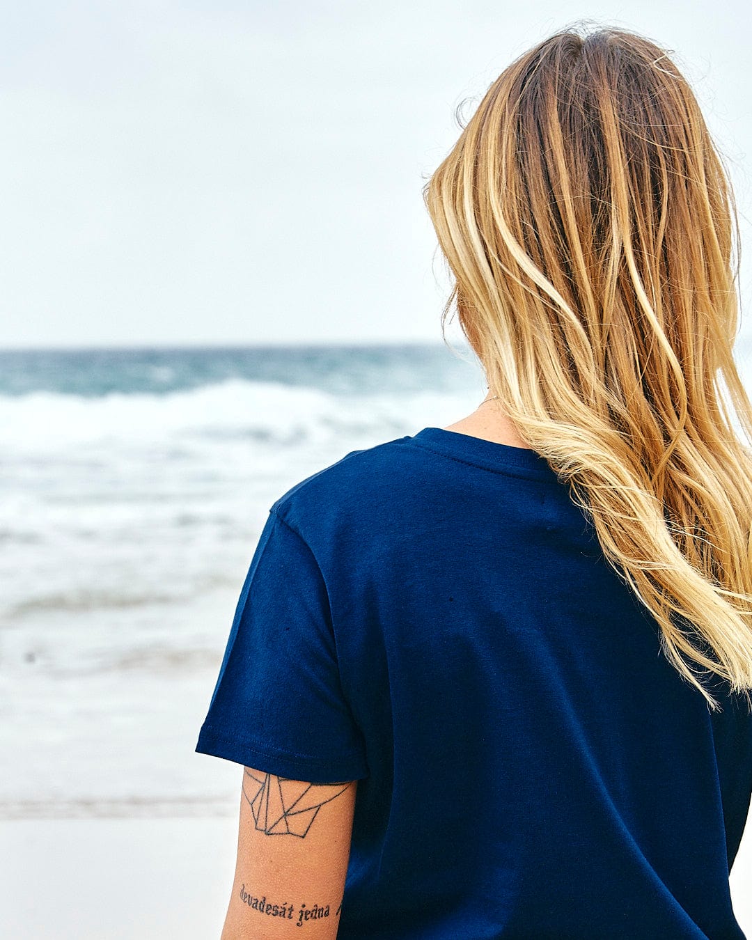 A woman sitting on the beach with her back to the ocean wearing the Saltrock Celeste Stripe - Womens Short Sleeve T-Shirt in Blue.