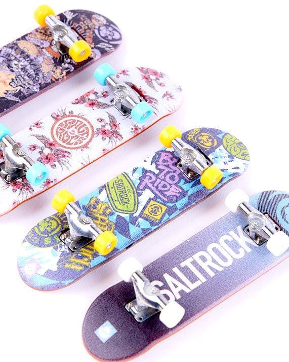 Four Saltrock Creeper Cruiser - Digit Deck - Black mini finger skateboards with different designs are lined up on a white surface.